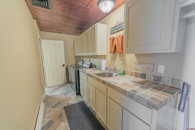 kitchen featuring washer and dryer, a baseboard heating unit, light tile floors, sink, and tile countertops