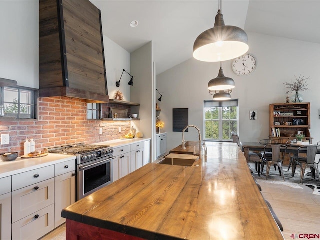 kitchen featuring high end stainless steel range oven, wood counters, hanging light fixtures, range hood, and sink