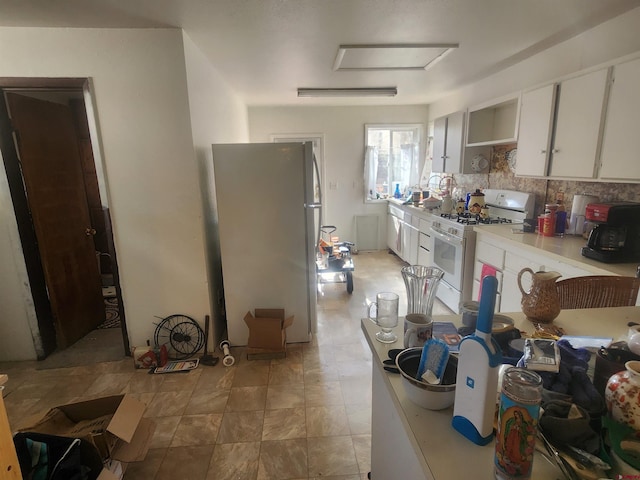 kitchen featuring white cabinetry, tasteful backsplash, white gas range oven, and refrigerator