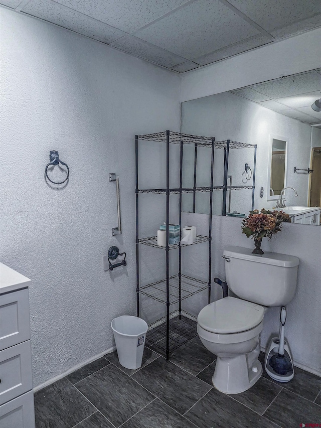 bathroom with tile flooring, a paneled ceiling, vanity, and toilet