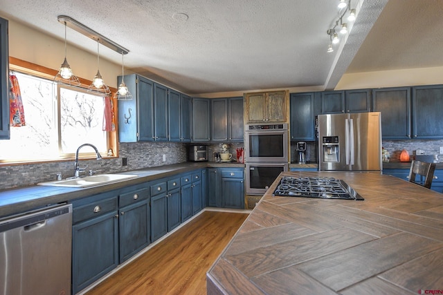 kitchen with a textured ceiling, stainless steel appliances, wooden counters, backsplash, and sink