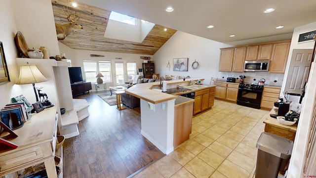 kitchen featuring black range, backsplash, light brown cabinetry, vaulted ceiling, and a breakfast bar area