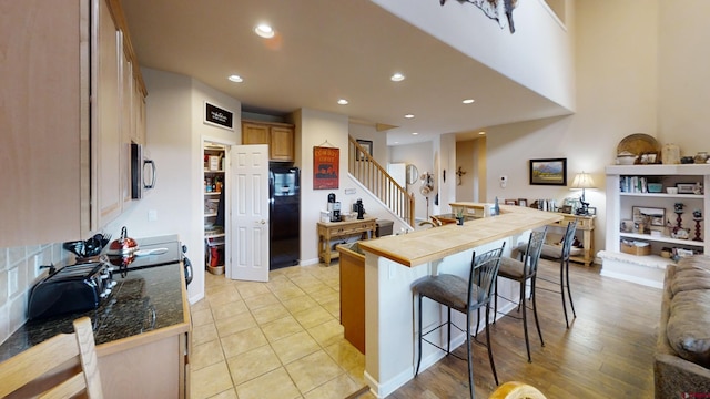 kitchen with black refrigerator, light brown cabinets, light tile floors, and a kitchen bar