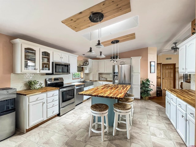 kitchen with a kitchen island, appliances with stainless steel finishes, white cabinets, and butcher block countertops