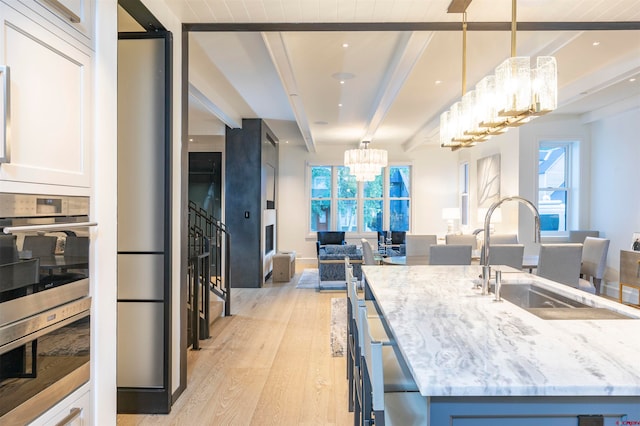 kitchen with an island with sink, beamed ceiling, decorative light fixtures, light wood-type flooring, and a wealth of natural light