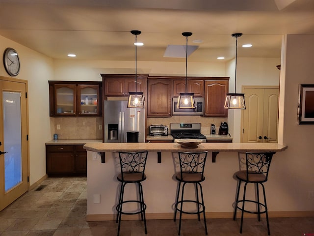 kitchen featuring a kitchen breakfast bar, stainless steel appliances, dark brown cabinetry, decorative light fixtures, and tasteful backsplash