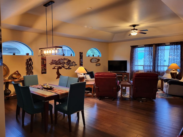 dining room with dark wood-type flooring, a tray ceiling, and ceiling fan