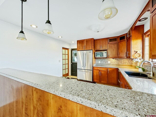 kitchen with light stone countertops, stainless steel appliances, decorative light fixtures, backsplash, and sink