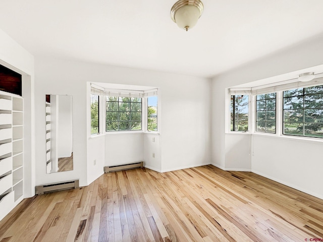 empty room featuring a baseboard heating unit, plenty of natural light, and light wood-type flooring