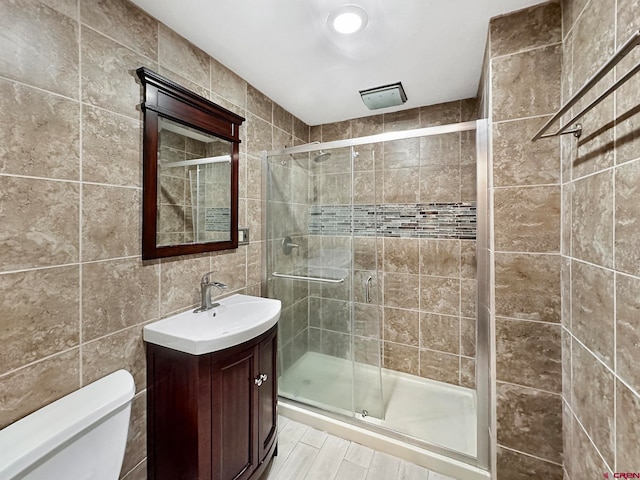 bathroom with a shower with shower door, vanity with extensive cabinet space, tile walls, and toilet