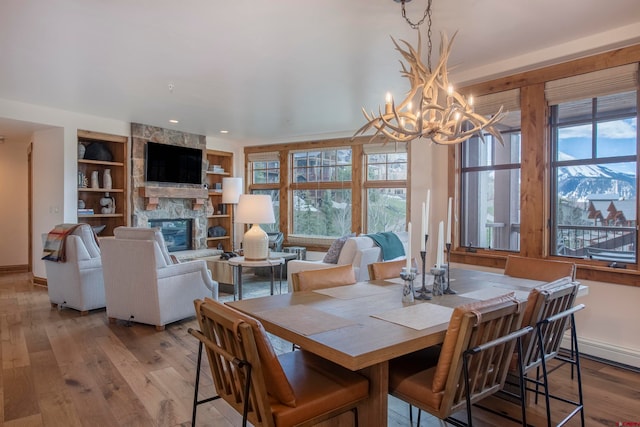 dining room with a stone fireplace, a wealth of natural light, built in shelves, and wood-type flooring