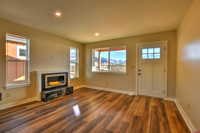 unfurnished living room featuring a glass covered fireplace, dark wood-style flooring, baseboards, and recessed lighting