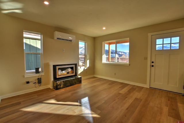 unfurnished living room with a high end fireplace, a wall unit AC, baseboards, and wood finished floors