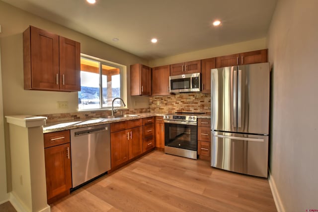 kitchen with brown cabinets, light wood finished floors, recessed lighting, appliances with stainless steel finishes, and a sink