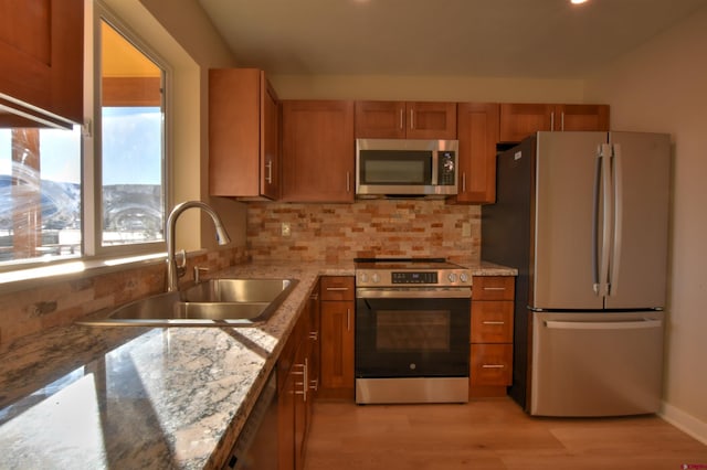 kitchen with brown cabinets, light wood finished floors, decorative backsplash, appliances with stainless steel finishes, and a sink