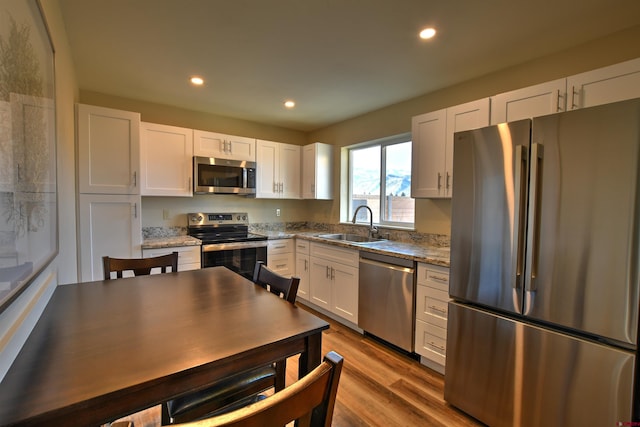 kitchen with recessed lighting, wood finished floors, a sink, white cabinets, and appliances with stainless steel finishes