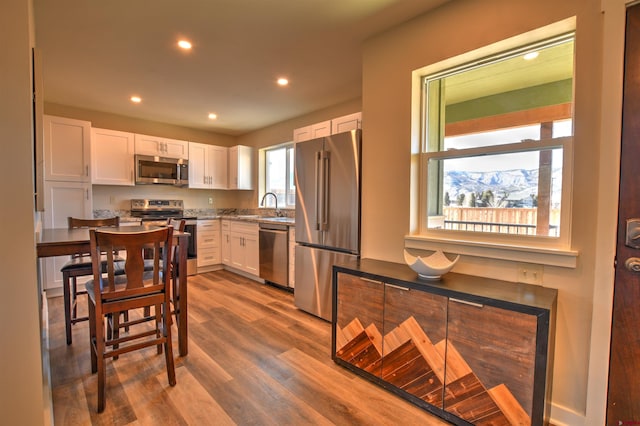 kitchen with recessed lighting, appliances with stainless steel finishes, white cabinets, a sink, and wood finished floors