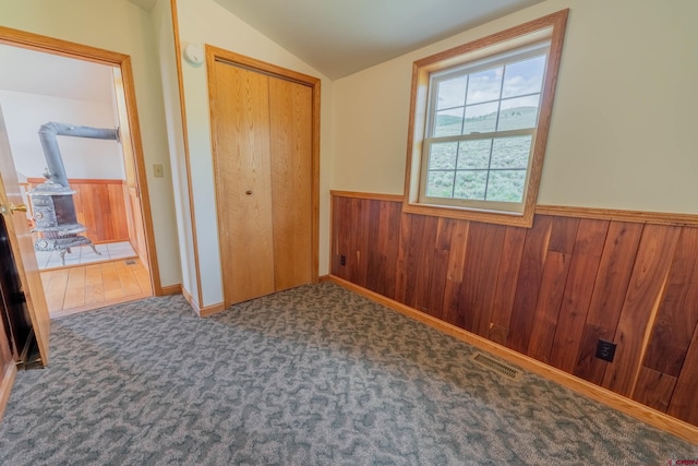 unfurnished bedroom with dark carpet, wooden walls, a closet, and lofted ceiling