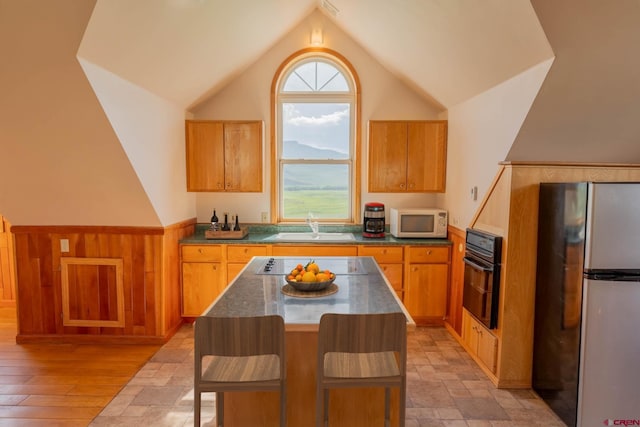 kitchen featuring a kitchen breakfast bar, a kitchen island, black appliances, sink, and vaulted ceiling