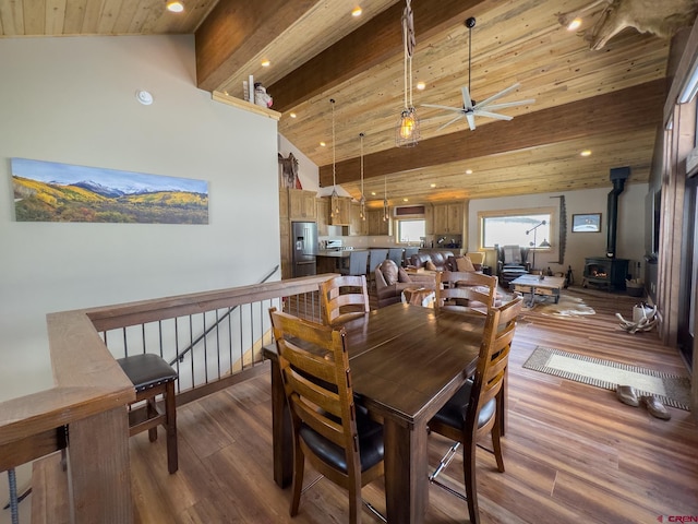 dining area featuring ceiling fan, hardwood / wood-style floors, wood ceiling, a wood stove, and high vaulted ceiling