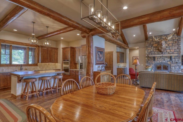 dining room with a stone fireplace, sink, vaulted ceiling with beams, and dark wood-type flooring