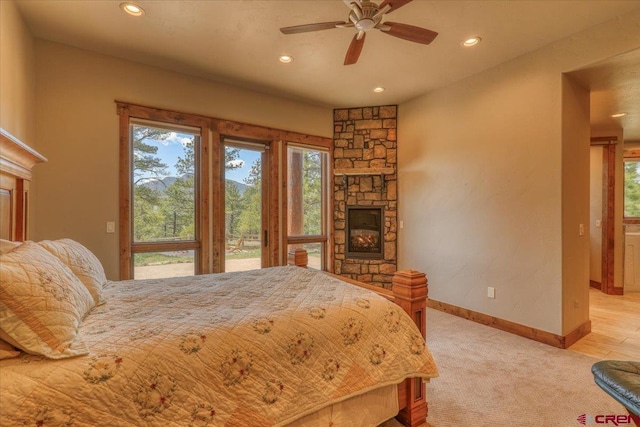 bedroom with light carpet, a stone fireplace, ceiling fan, and access to outside