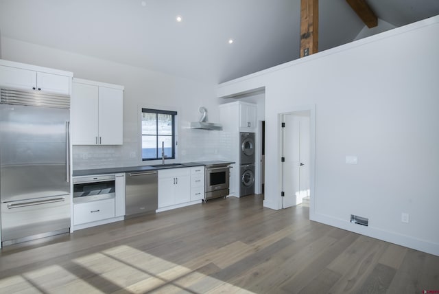 kitchen featuring white cabinets, backsplash, stainless steel appliances, and stacked washer / dryer