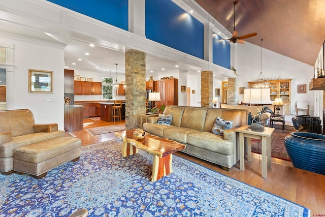 living room with ceiling fan, crown molding, ornate columns, wood-type flooring, and a towering ceiling