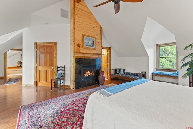 bedroom with a fireplace, ceiling fan, high vaulted ceiling, wood-type flooring, and wooden walls