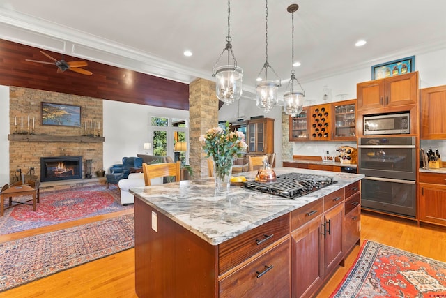 kitchen with stainless steel appliances, a fireplace, light wood-type flooring, and ceiling fan with notable chandelier