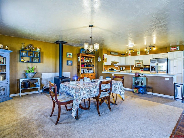 dining space with a textured ceiling, a wood stove, sink, a chandelier, and light colored carpet