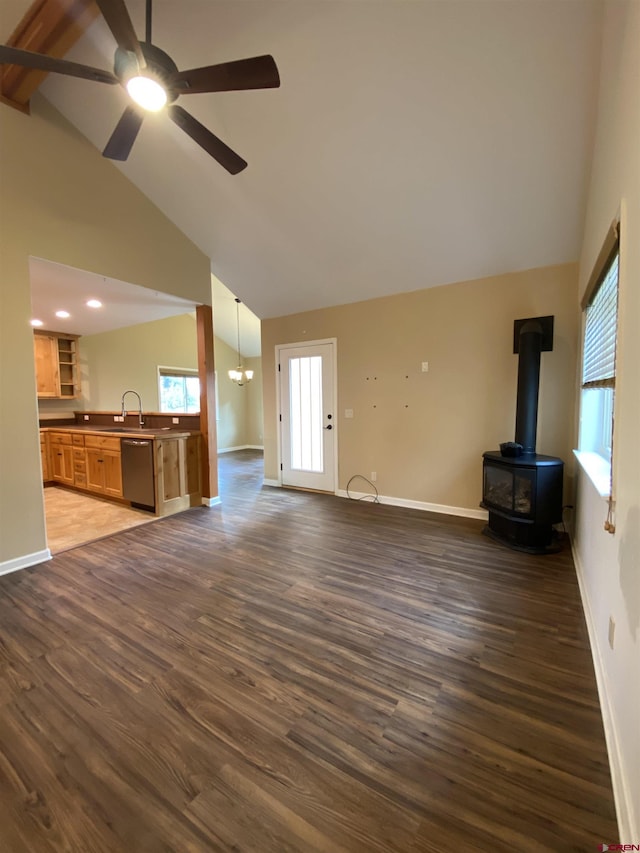 unfurnished living room with a wood stove, sink, high vaulted ceiling, dark hardwood / wood-style floors, and ceiling fan with notable chandelier