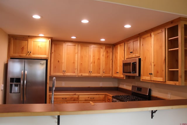 kitchen featuring a kitchen bar, kitchen peninsula, light brown cabinetry, and appliances with stainless steel finishes