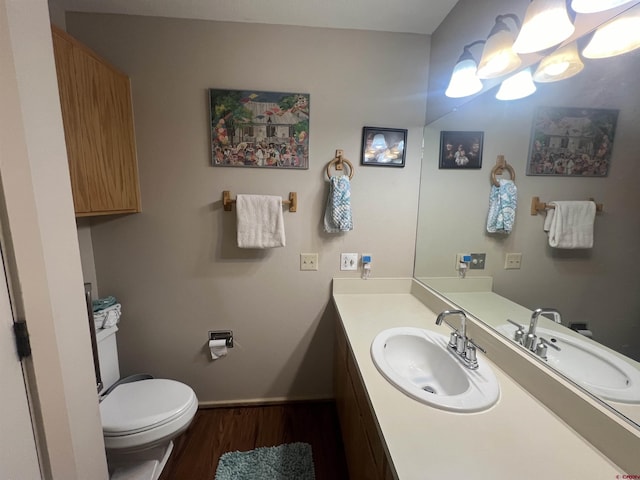 bathroom with toilet, wood finished floors, vanity, and baseboards