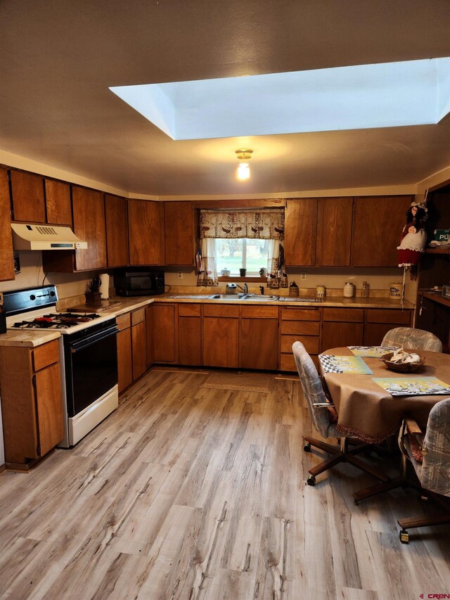 kitchen with gas range gas stove, sink, light wood-type flooring, and a skylight