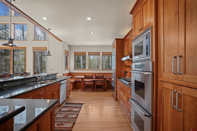 kitchen with appliances with stainless steel finishes, dark stone counters, sink, pendant lighting, and light hardwood / wood-style flooring