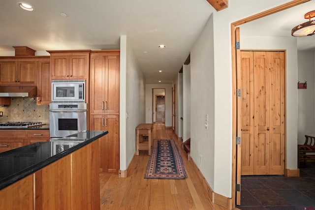 kitchen featuring hardwood / wood-style floors, dark stone counters, tasteful backsplash, stainless steel appliances, and extractor fan