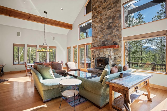 living room with a high ceiling, light wood-type flooring, a stone fireplace, and a healthy amount of sunlight