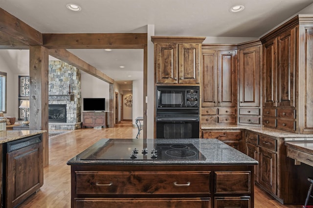 kitchen featuring a center island, dark stone countertops, a fireplace, black appliances, and dark brown cabinets