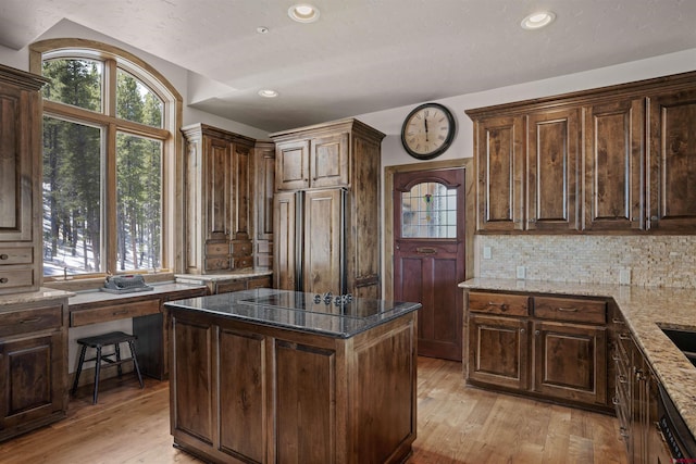 kitchen with a center island, light hardwood / wood-style floors, light stone counters, and dark brown cabinetry