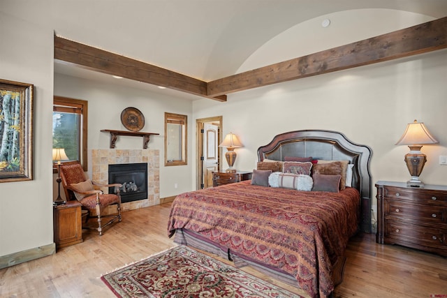 bedroom with a tile fireplace, light wood-type flooring, and vaulted ceiling