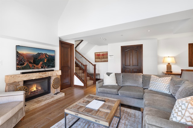 living room featuring a stone fireplace, vaulted ceiling, and hardwood / wood-style flooring