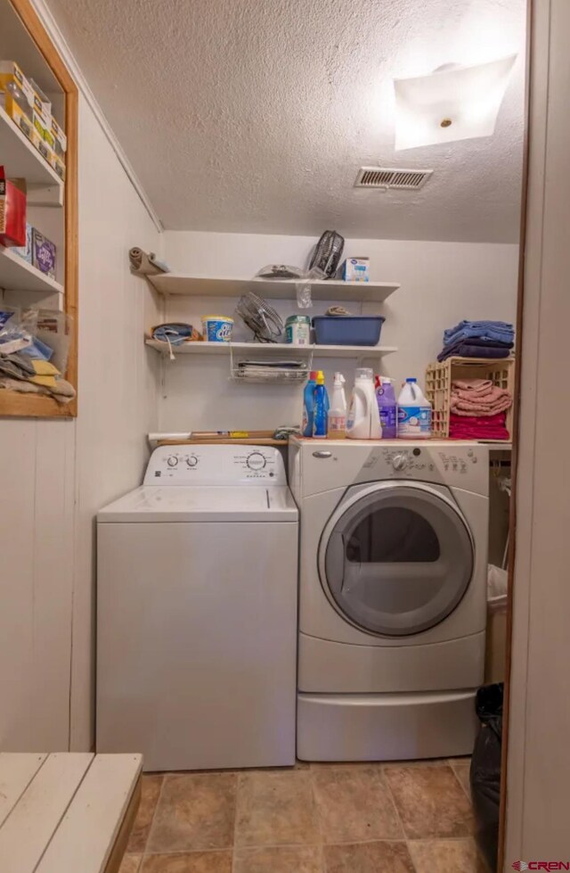 clothes washing area with washing machine and dryer, a textured ceiling, and light tile floors