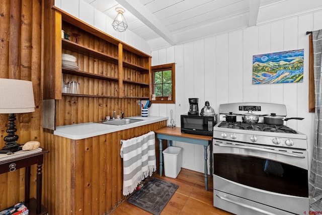 kitchen featuring beam ceiling, sink, gas stove, and wood walls