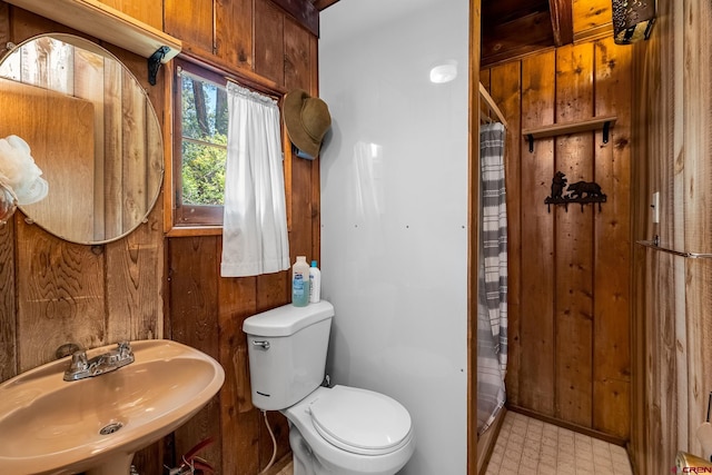 bathroom with tile flooring, a shower with shower curtain, wood walls, sink, and toilet