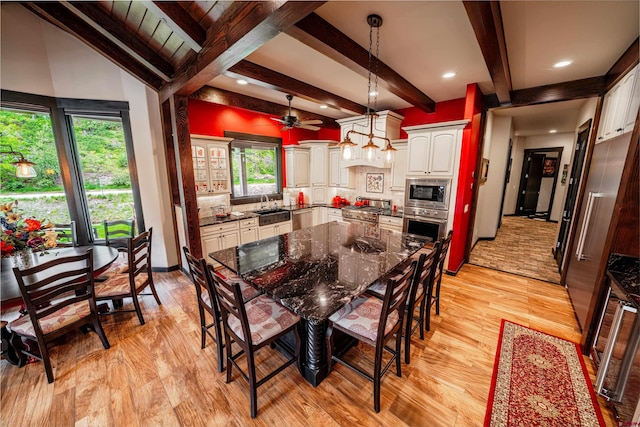 dining space with ceiling fan, lofted ceiling with beams, light wood-type flooring, and sink