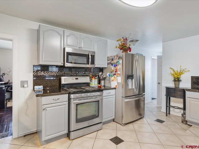 kitchen featuring dark stone counters, backsplash, light tile floors, and stainless steel appliances