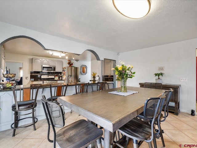 dining room featuring rail lighting, a textured ceiling, and light tile floors