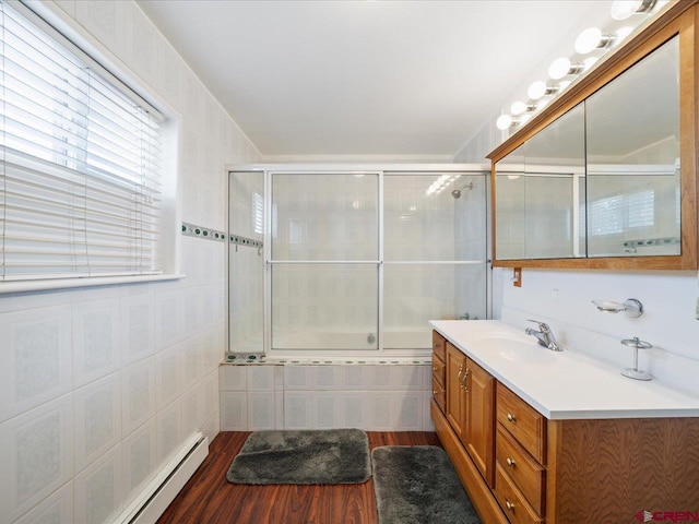 bathroom featuring tile walls, enclosed tub / shower combo, hardwood / wood-style floors, baseboard heating, and vanity