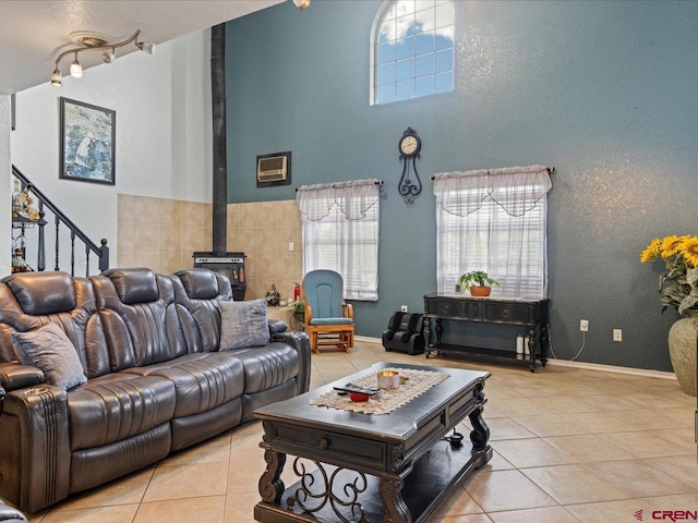 living room with a textured ceiling, a high ceiling, a wood stove, rail lighting, and light tile flooring